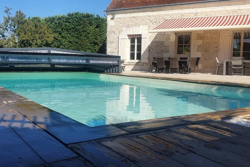 una piscina con acqua blu di fronte a una casa di Longère avec Piscine Couverte Chauffée privative de Avril à Septembre a Luzillé