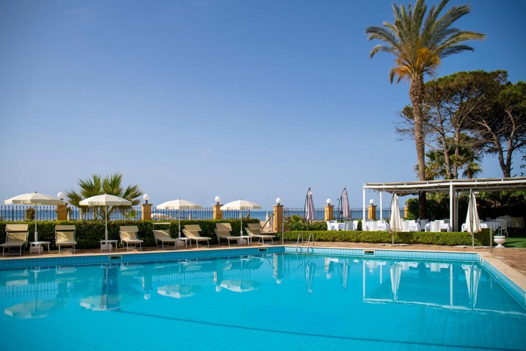 een groot blauw zwembad met stoelen en palmbomen bij Hotel Villa Romana in Porto Empedocle