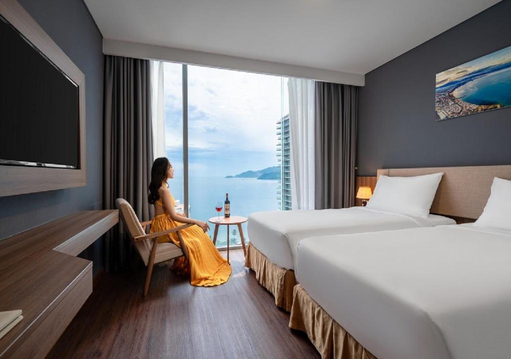 a woman sitting in a chair in a hotel room with two beds at Libra Hotel Nha Trang in Nha Trang