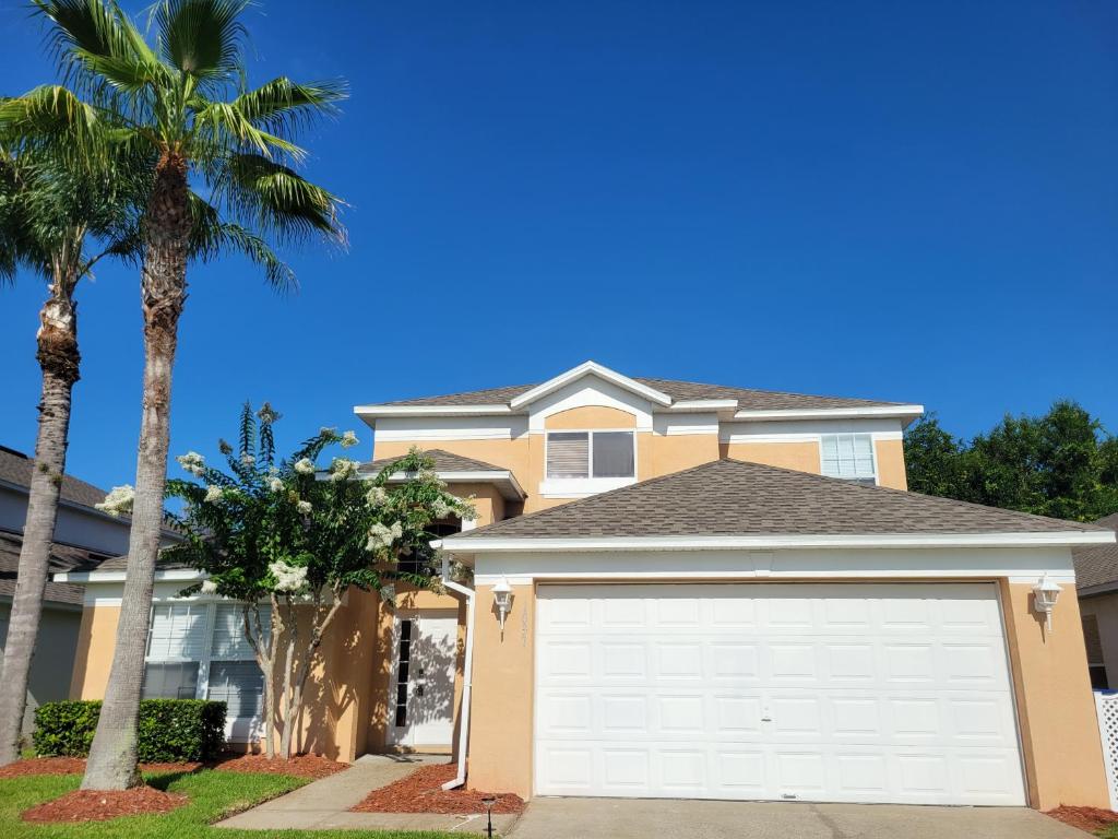 a house with a white garage door and a palm tree at Fully Renovated, Quiet, Spacious Disney Themed Pool Home with Office in Kissimmee