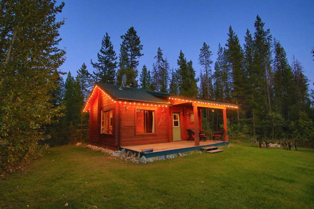 une petite cabane en rondins avec des lumières allumées dans un champ dans l'établissement Mica Mountain Lodge & Log Cabins, à Tête Jaune Cache