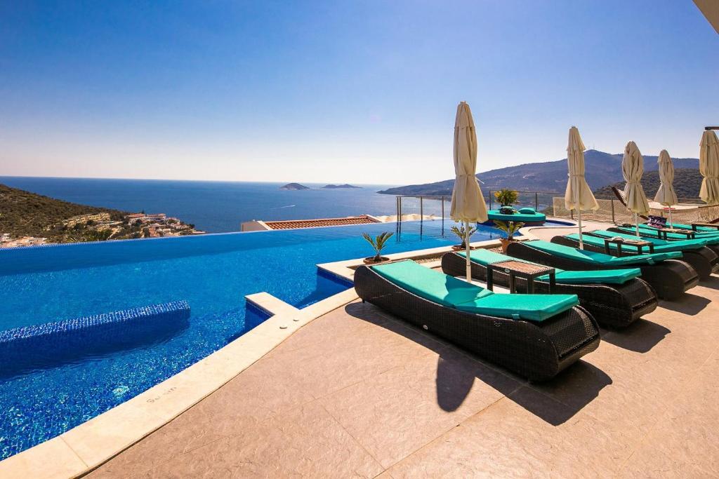 a pool with lounge chairs and umbrellas and the ocean at Villa Pırlanta, Kalkanvilla in Kalkan