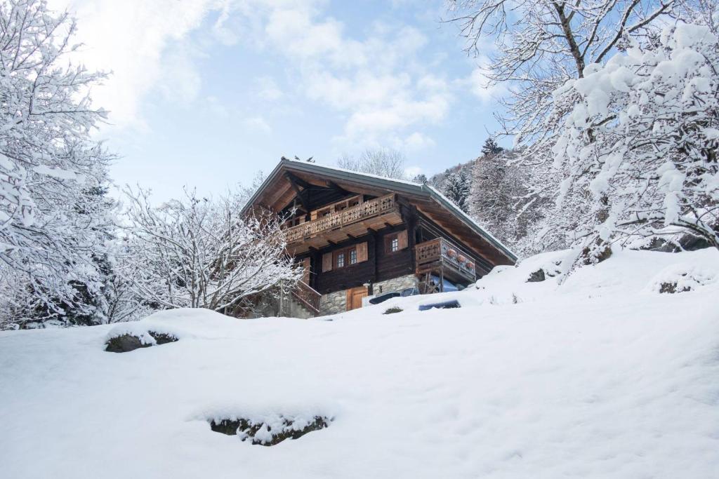 una baita di tronchi nella neve con alberi di Les Quatre Saisons - balcon et jardin a Val-d'Illiez