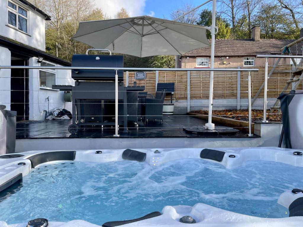 a hot tub on a patio with an umbrella at Tollgate House - Luxury Cozy Cottage - HUGE Hot Tub - Alton Towers in Cheadle