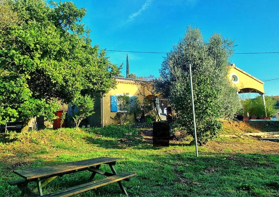 un banco de madera sentado en el césped frente a una casa en Villa Mistral - Profitez du calme de l'Ardèche - 