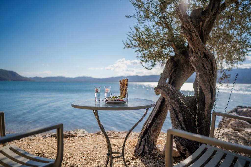 a table and chairs next to a tree next to the water at Beautiful Traditional Stone House in the private Sea Front Olive Grove of Elaionas Nikou Luxury Villas in Alyfantá