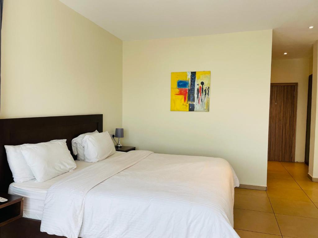 Un dormitorio con una cama blanca y una pintura en la pared en New Brookfields Hotel, en Freetown