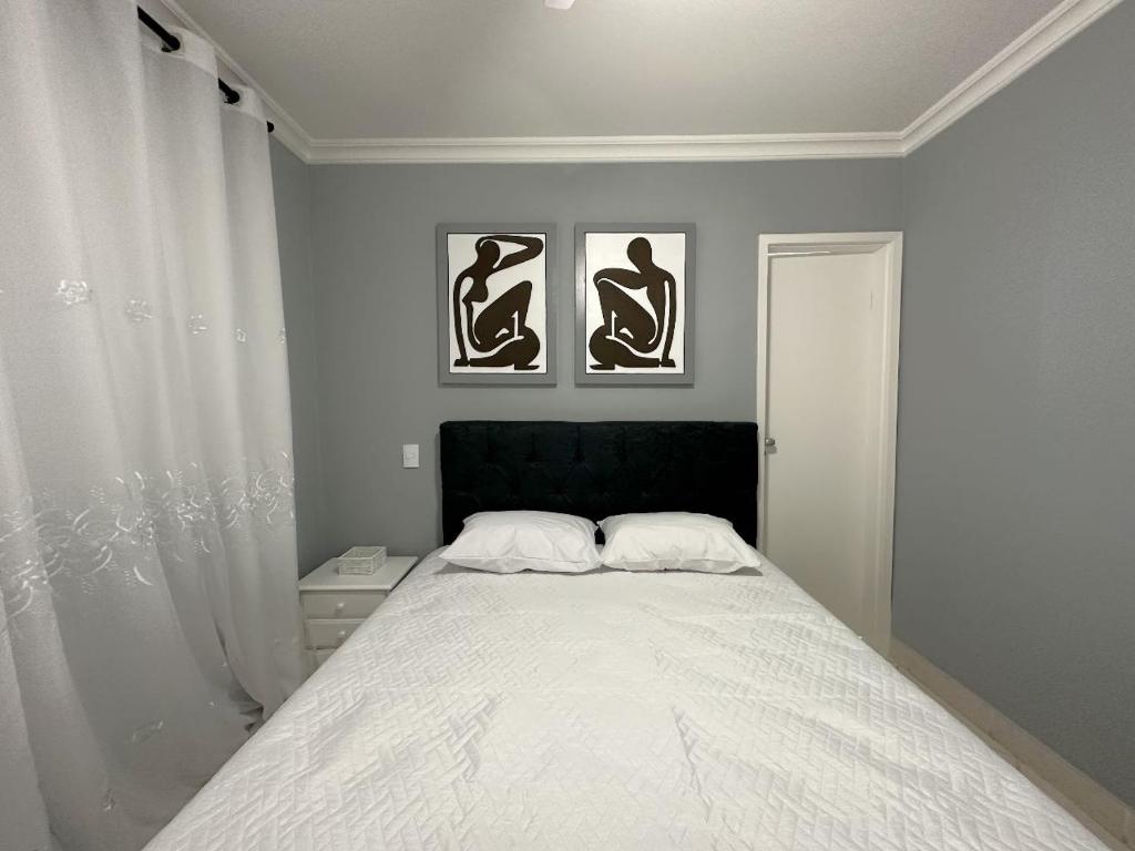 ein Schlafzimmer mit einem Bett mit drei Bildern an der Wand in der Unterkunft Pé na Areia a Poucos Metros -Apartamento Guarujá Pitangueiras in Guarujá