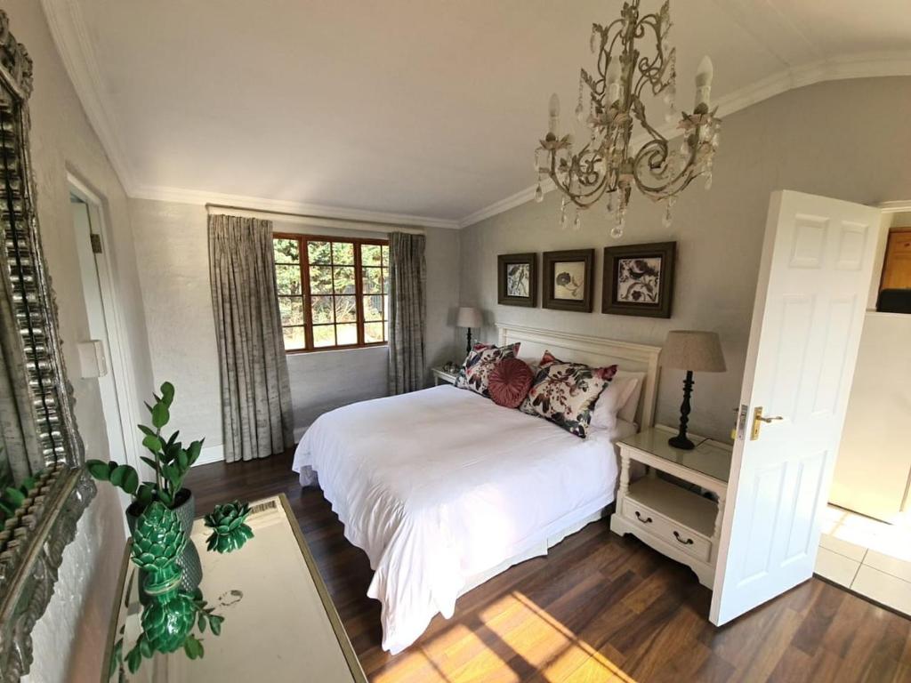 a bedroom with a white bed and a chandelier at The Falls Cottages in Balgowan