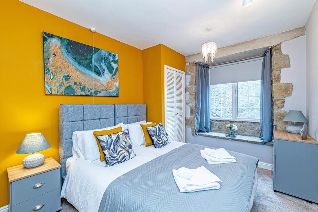 a bedroom with two beds with yellow walls and a window at Bridge End Mill Apartments In Settle in Settle