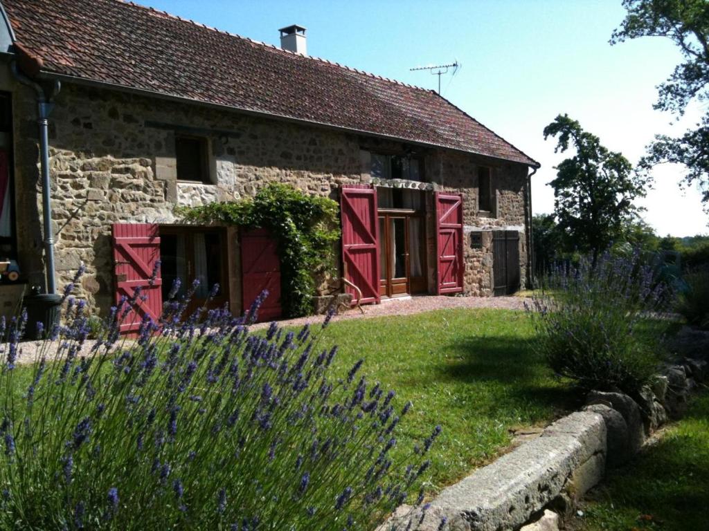 uma antiga casa de pedra com portas vermelhas e flores roxas em Gîte Beaune-d'Allier, 4 pièces, 6 personnes - FR-1-489-246 em Beaune dʼAllier