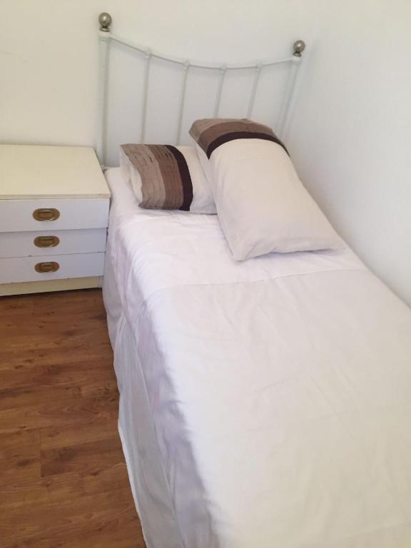 Devons Unique Short Stay في لندن: سرير بشرشف ووسائد بيضاء في غرفة النوم