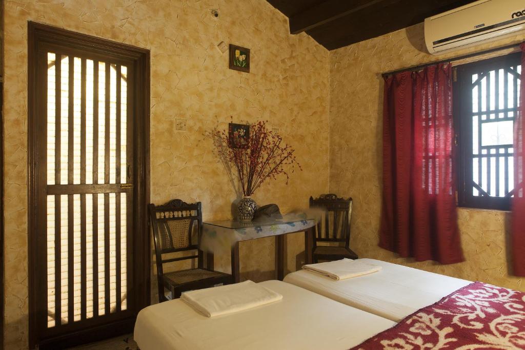 a bedroom with two beds and a table and windows at Afonso Guest House in Panaji