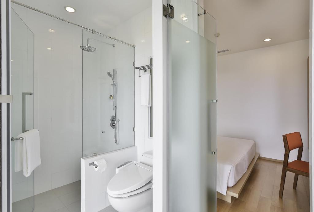 A compact glass shower room with a toilet and a glimpse of the adjacent bedroom.