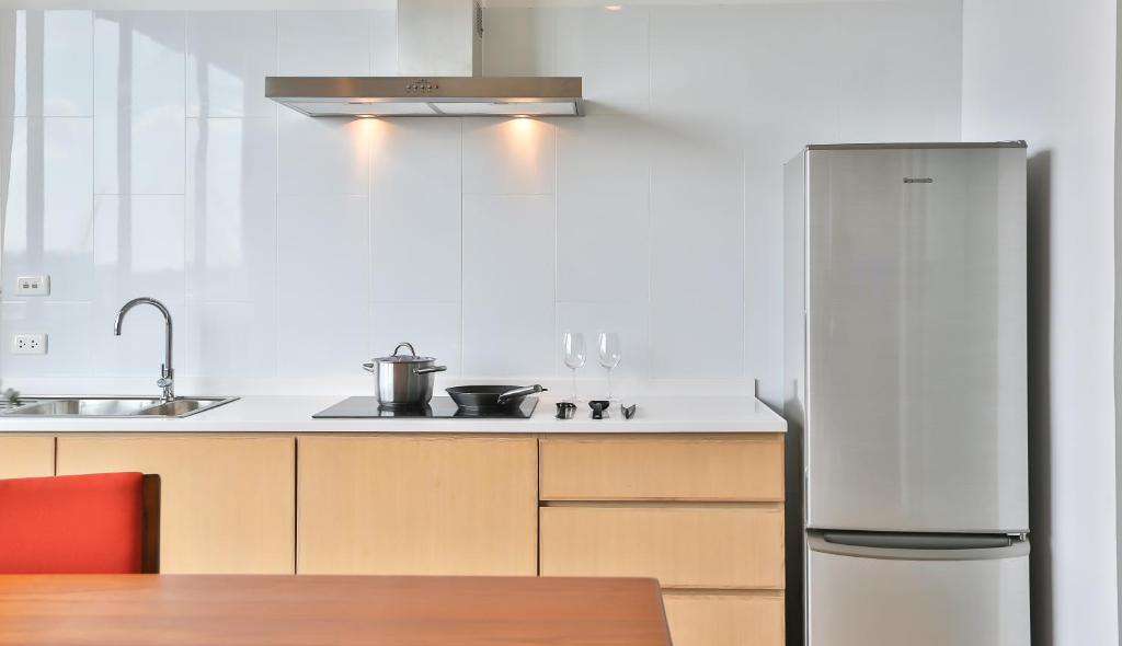 A compact apartment kitchen with a sink, induction hob, hood, cabinets, and full-height refrigerator.