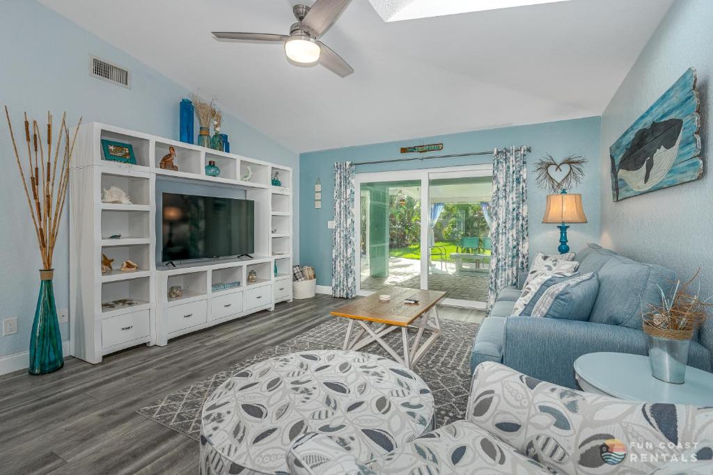 a living room with a blue couch and a tv at Relaxing Beach Home with Fire Pit and Private Fenced Yard STEPS from the Sand! in New Smyrna Beach