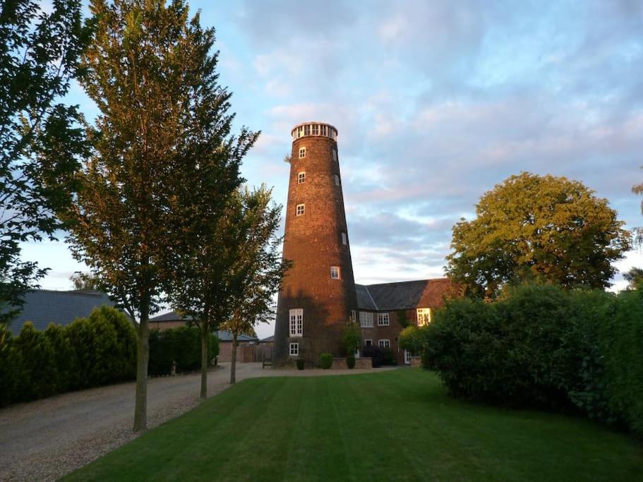 un edificio con una torre de ladrillo en medio de un patio en The Old Mill, 7 storey,, dog friendly outdoor pool & bbq, en Stoke Ferry