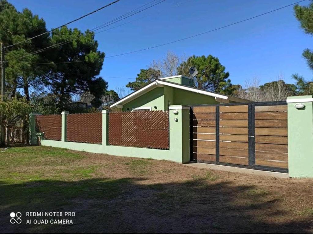 una valla con una puerta de madera frente a una casa en Chalet de 2 dorm- 1baño - Piscina en Valeria del Mar