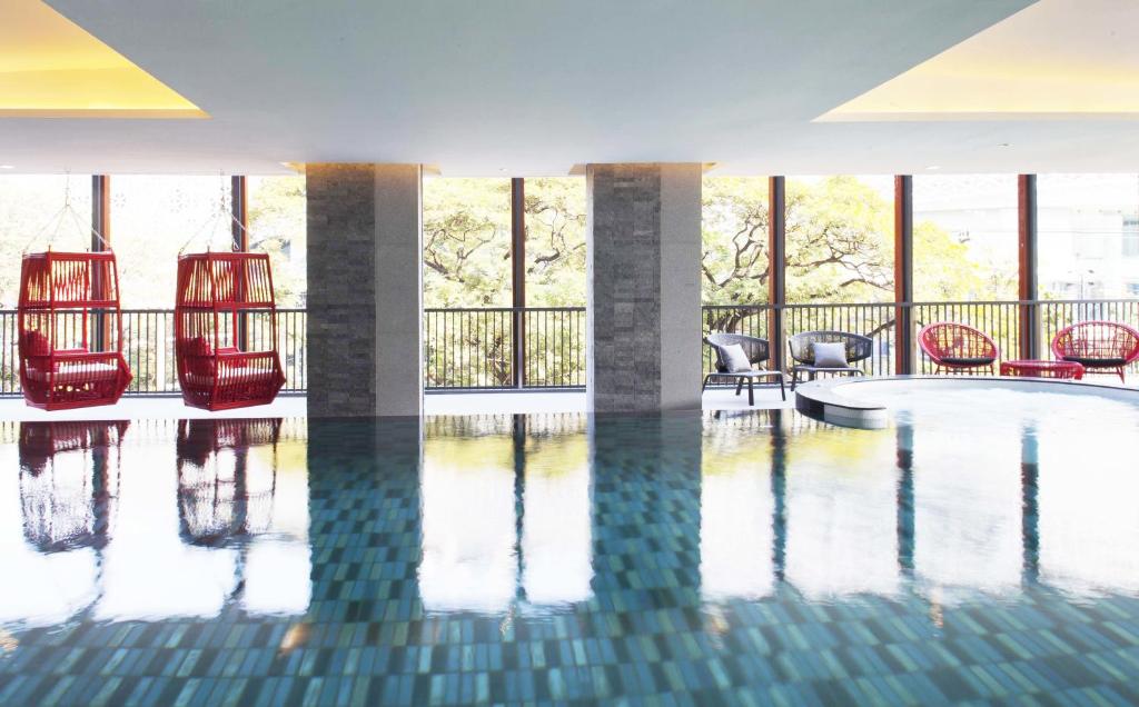 An indoor pool sits beside floor-to-ceiling windows, red hanging chairs, and a small cluster of loungers.