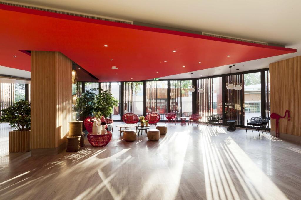 A spacious lobby lounge with a red ceiling, timber walls, and plentiful seating by the windows.