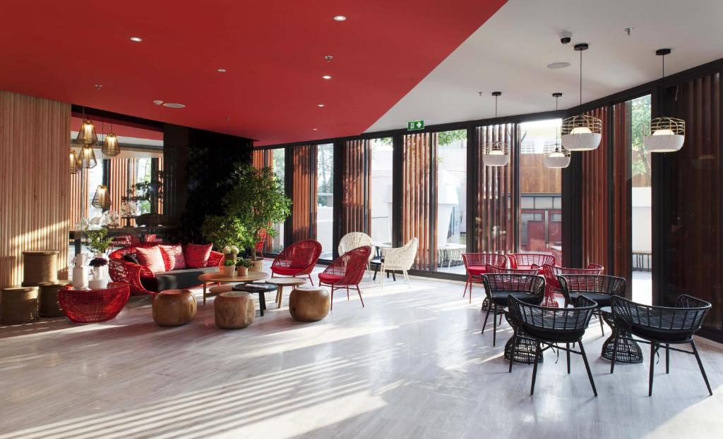 A colorful lobby lounge with red seating, café tables and tall windows.