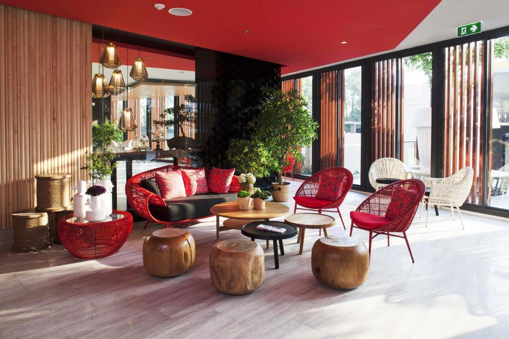 A colorful lobby lounge combines red chairs, a sofa, wood tables, and bright windows.