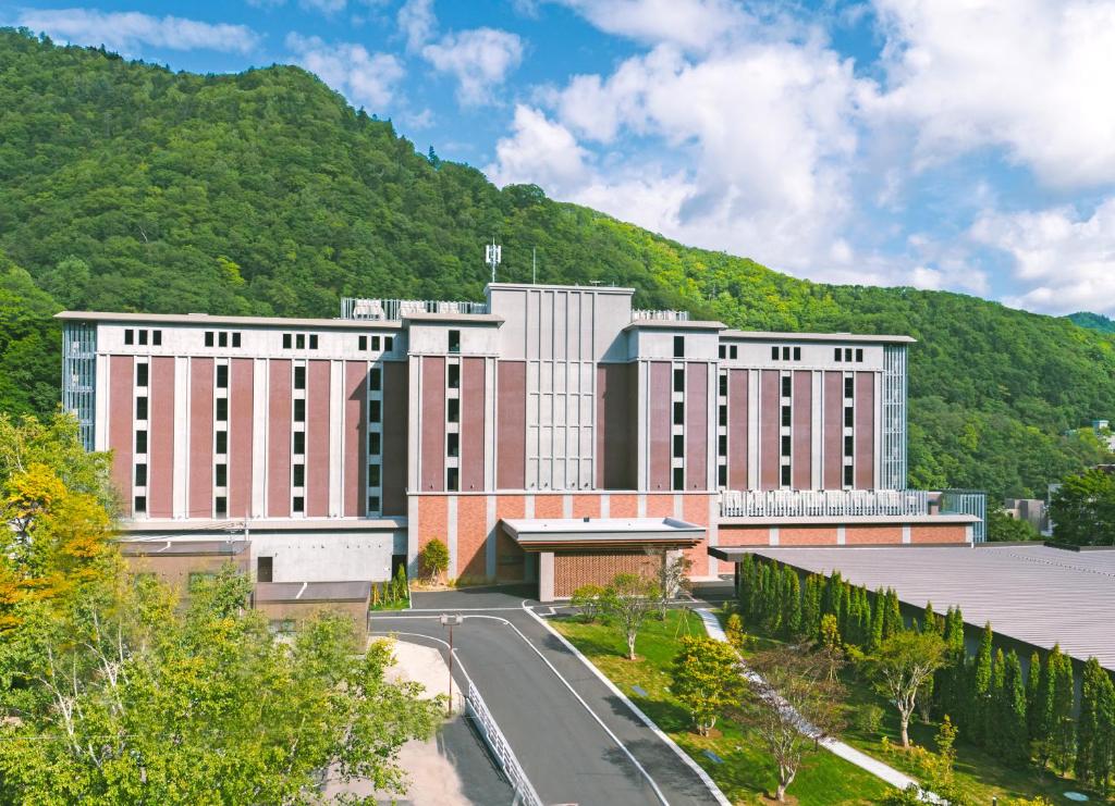 a large building with a road in front of a mountain at Grand Blissen Hotel Jozankei in Jozankei