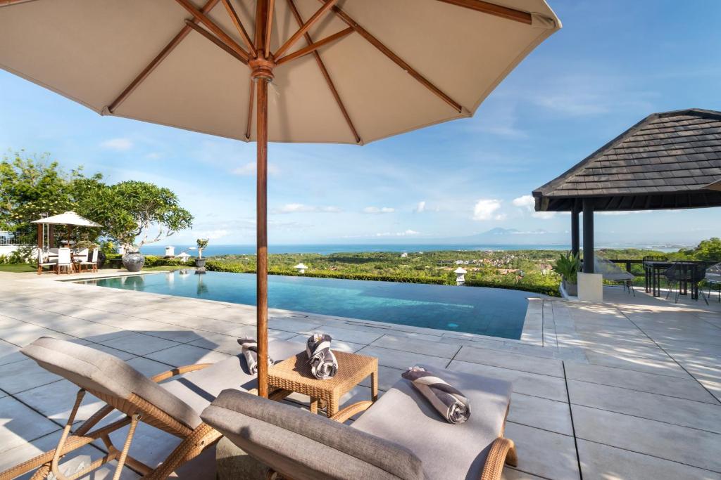 a patio with chairs and an umbrella and a swimming pool at Villa Puri Balangan in Uluwatu