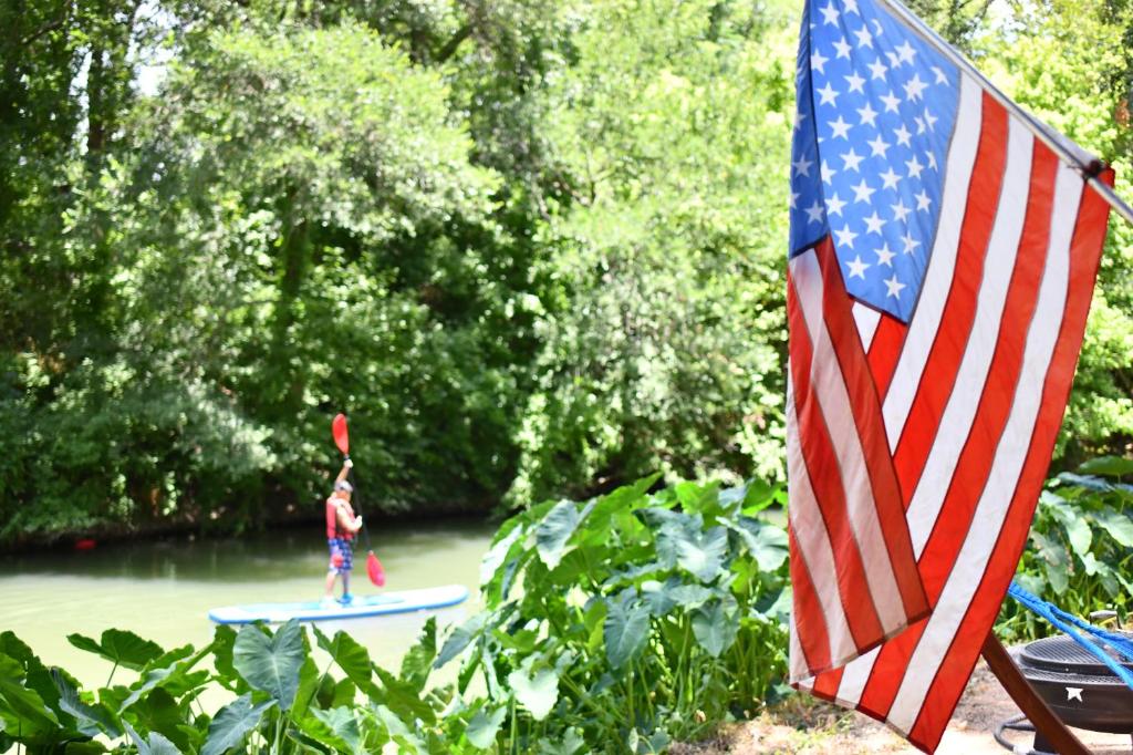 a person on a surfboard next to an american flag at Son's Rio Cibolo Glamping Cabin #G Brand New Creek-front Cabins with SO Many Amenities! in Marion