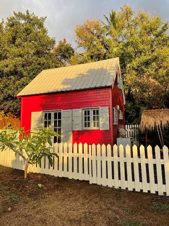 a red house behind a white fence at La Petite Kaz Dans la Savane in Fleurimont