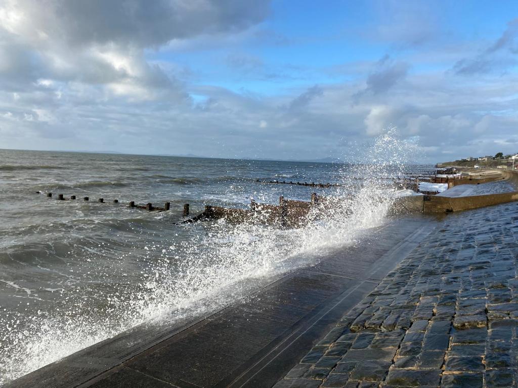 a large splash of water on a sidewalk next to the ocean at No40Barmouth-Modern,Spacious&Hot Tub in Barmouth