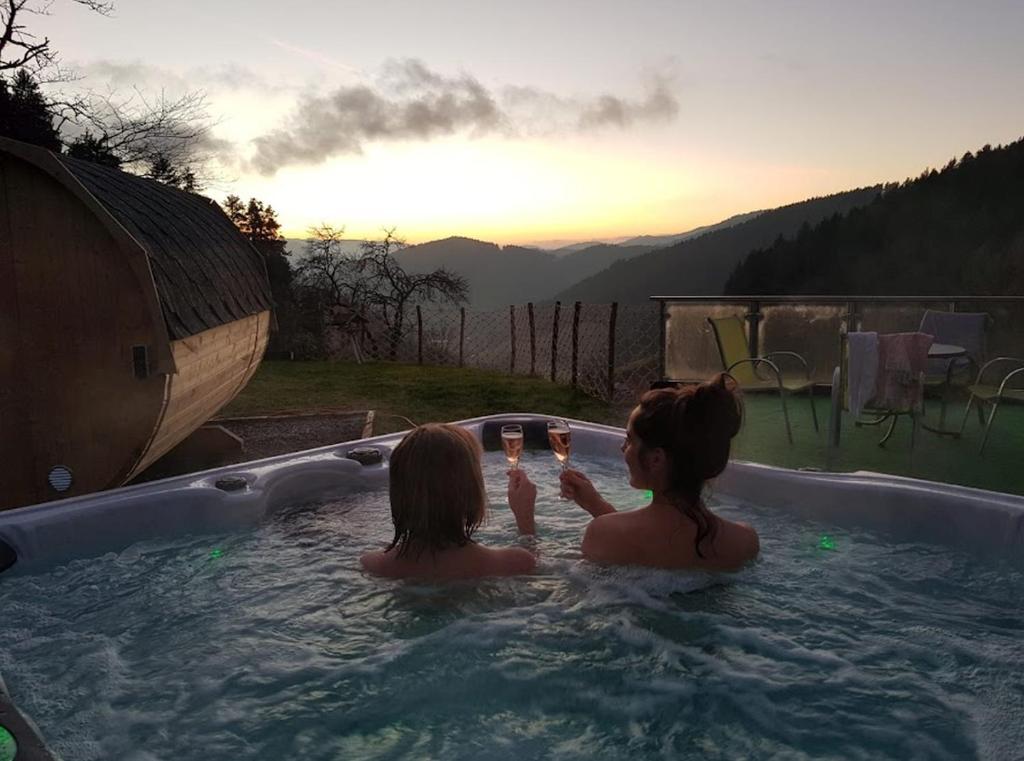 Duas raparigas sentadas numa banheira com o pôr-do-sol em Ferienhaus Wendelinus mit Pool & Sauna em Hausach