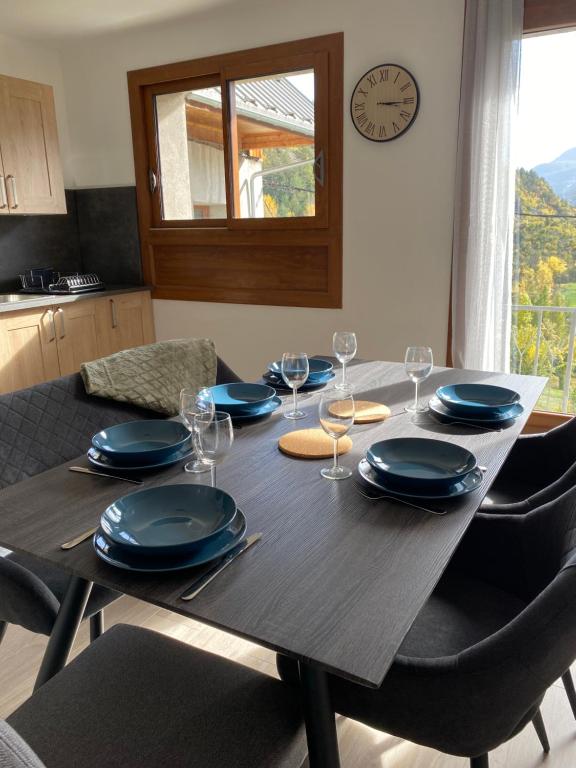 a dining room table with plates and glasses and a clock at Appartement Le Lauzet in La Roche-de-Rame