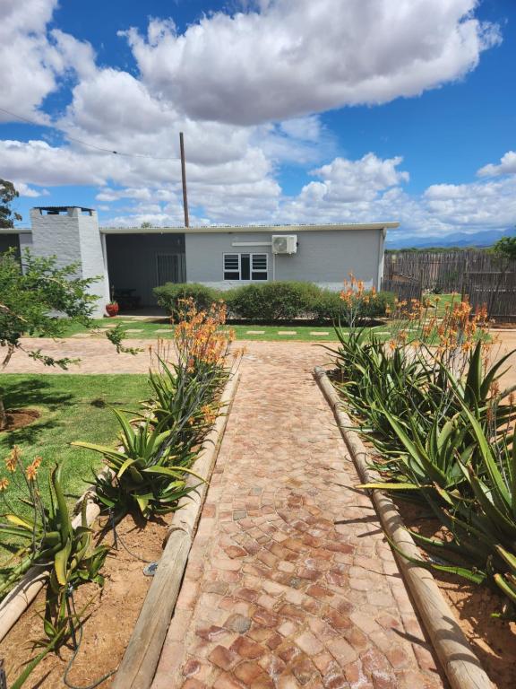 a house with a brick walkway in front of a yard at Volgenoeg Self Catering in Oudtshoorn