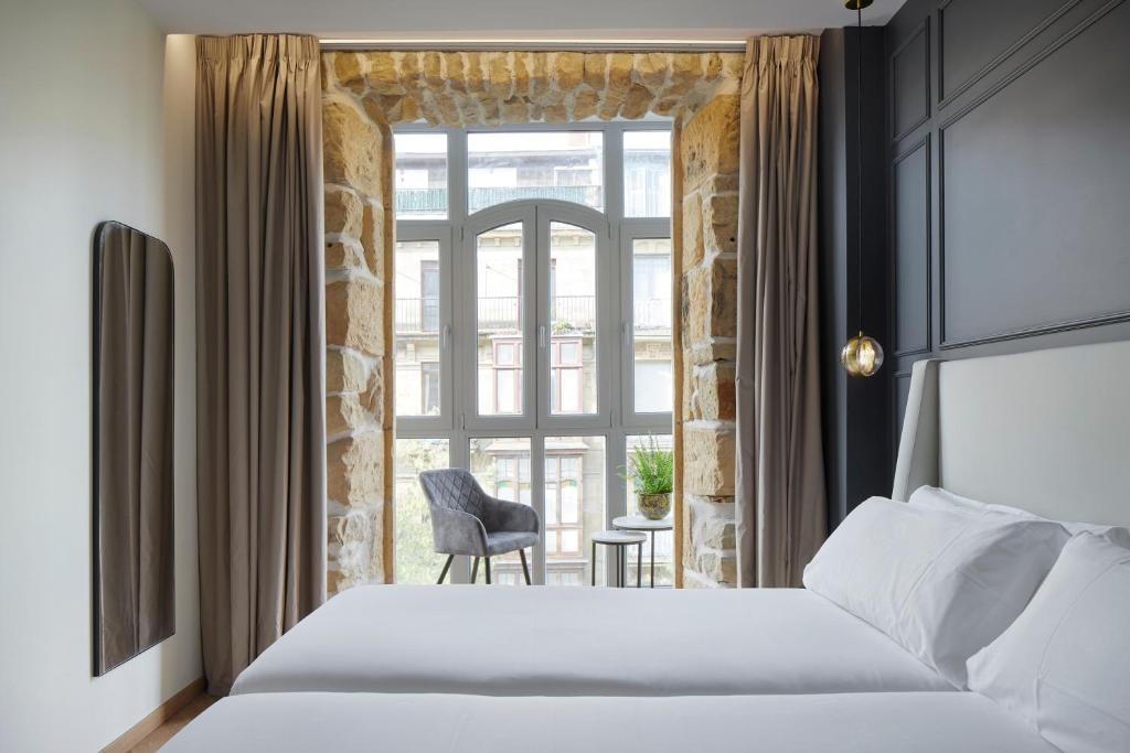 Schlafzimmer mit einem Bett und einem Fenster mit einem Stuhl in der Unterkunft HOTEL ARRIZUL CATEDRAL in San Sebastián