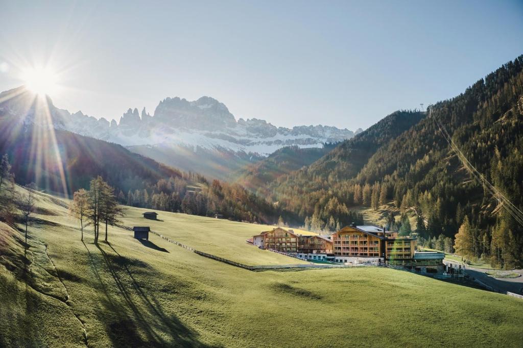 Cyprianerhof Dolomit Resort في تيريس: مبنى على تلة عشبية مع جبال في الخلفية