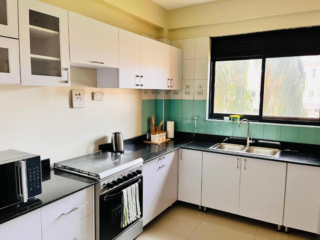 cocina con armarios blancos, fregadero y ventana en Spacious 3 Bedroom Apartment Excellent Location Bugolobi Kampala - Immersion 1 en Kampala