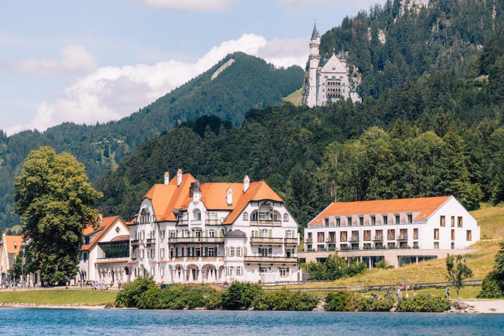 un gran edificio a orillas de un lago con un castillo en AMERON Neuschwanstein Alpsee Resort & Spa, en Schwangau