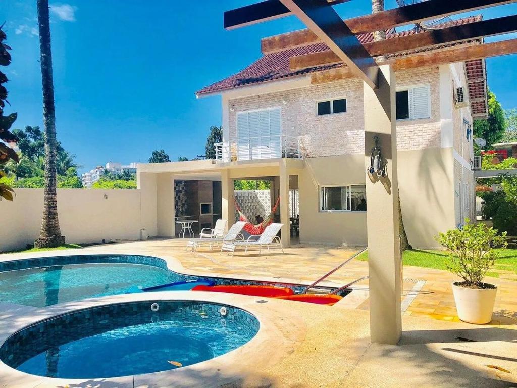 a villa with a swimming pool in front of a house at Casa para familia em Riviera, com WiFi in Bertioga
