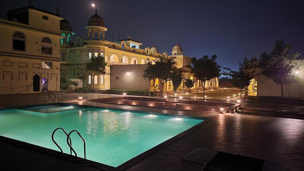 a swimming pool in front of a building at night at The Grand Barso (A Luxury Heritage) in Bharatpur