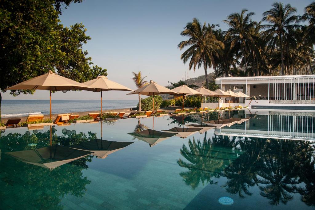 einen Pool mit Sonnenschirmen und Stühlen sowie das Meer in der Unterkunft Living Asia Resort and Spa in Senggigi 