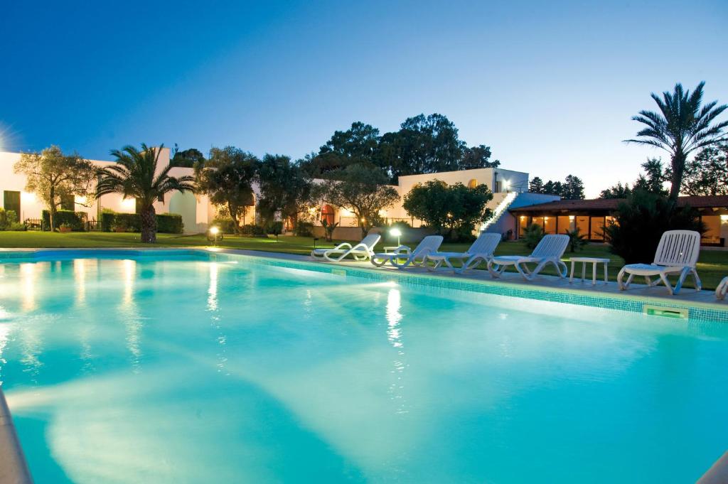 une grande piscine avec des chaises blanches et des arbres dans l'établissement Tenuta Badessa, à Casalabate