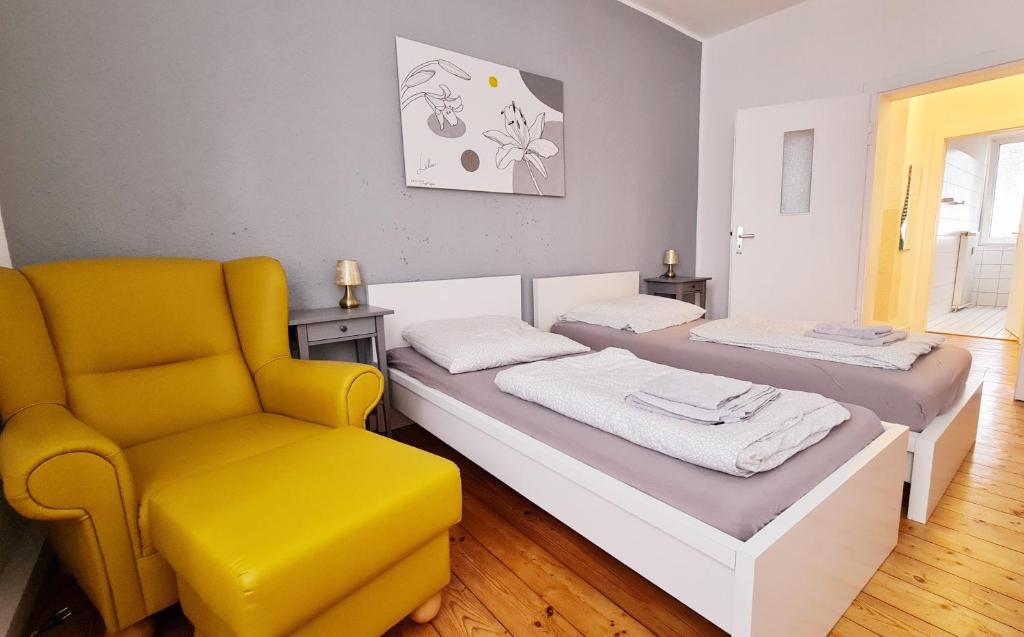 Cette chambre comprend deux lits et une chaise jaune. dans l'établissement ELENA flat LILIE, Oberhausen Zentrum CentrO Westfield, à Oberhausen