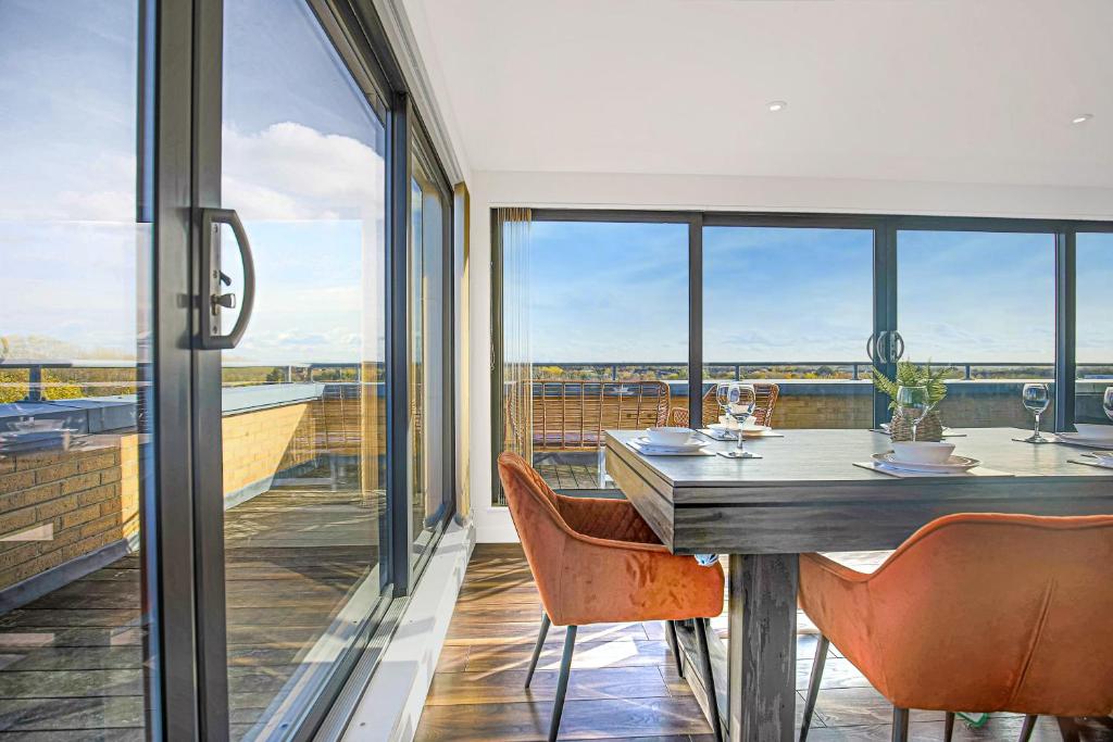a dining room with a table and chairs and windows at Luxury Penthouse Apartment - Central MK - Pool Table, Balcony, Fast WiFi, Free Parking and Smart TVs with Sky TV and Netflix by Yoko Property in Milton Keynes