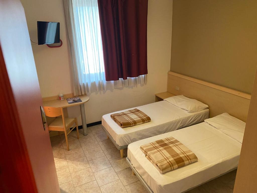a room with two beds and a table and a window at Hotel Mazzini in Lido di Jesolo