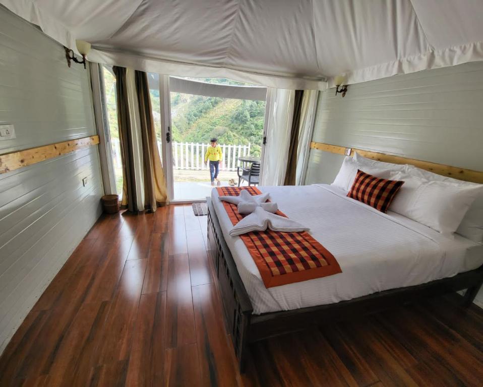 a bedroom with a large white bed with a person walking outside at Nature Waterfall Resort, Bir in Chauntrā