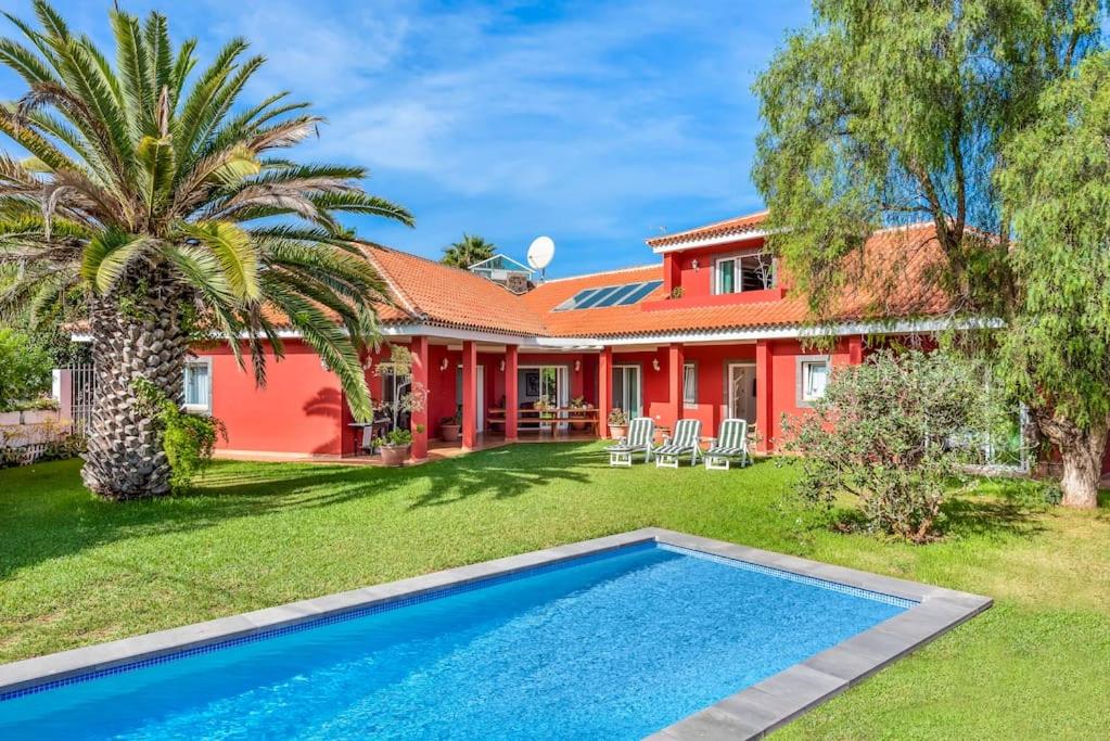 uma casa vermelha com uma palmeira e uma piscina em Villa Artigar, garden, swimming pool and bbq. em Puerto de la Cruz