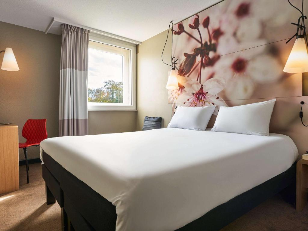 um quarto de hotel com uma grande cama branca com flores na parede em ibis Paris Marne la Vallee Emerainville em Émerainville