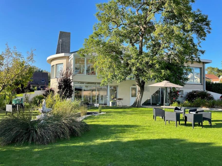 a house with chairs and an umbrella in the grass at Grande Villa de 8 chambres avec Balnéothérapie- Vill'Acacia in Bray-Dunes