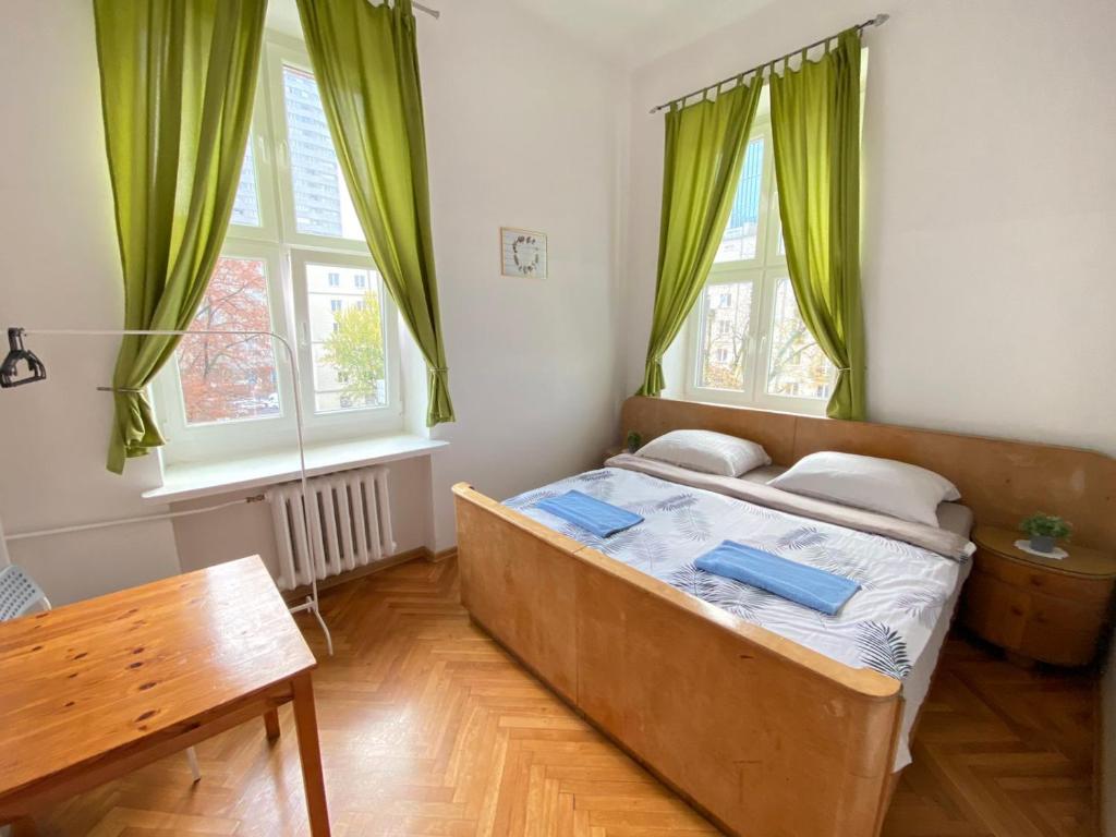 1 dormitorio con 1 cama con cortinas verdes y mesa en Oliwka Hostel, en Varsovia